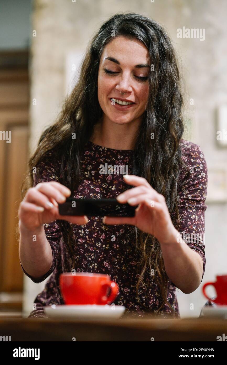 Young woman with some gray hair taking a photograph with her smartphone in a cafe bar.. Young woman with some gray hair using smartphone in a cafe. Stock Photo