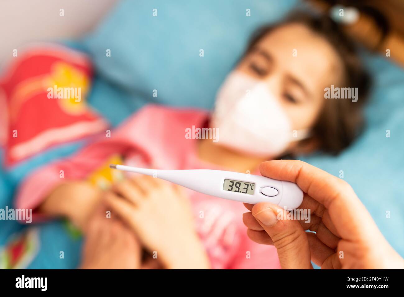 Mother measuring her toddler’s temperature, protected by a mask, with a