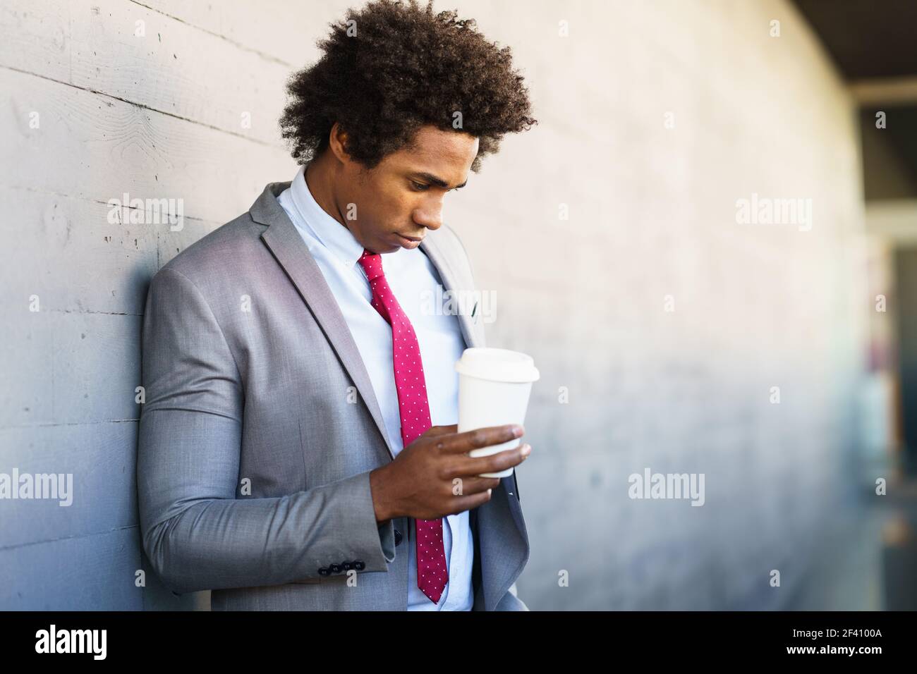 Worried Black Businessman taking a coffee break with a take-away glass. Man with afro hair.. Worried Black Businessman taking a coffee break outdoors Stock Photo