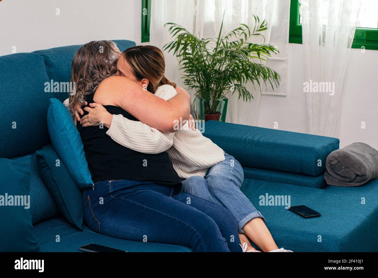 Elderly mother and young daughter cuddle affectionately on the sofa at home Stock Photo