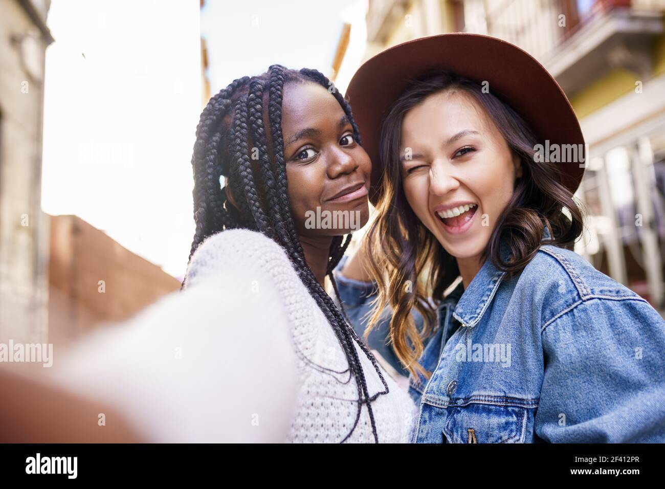 Two multiethnic women making selfie and grimacing with a smartphone.. Two beautiful multiethnic women making selfie and grimacing Stock Photo