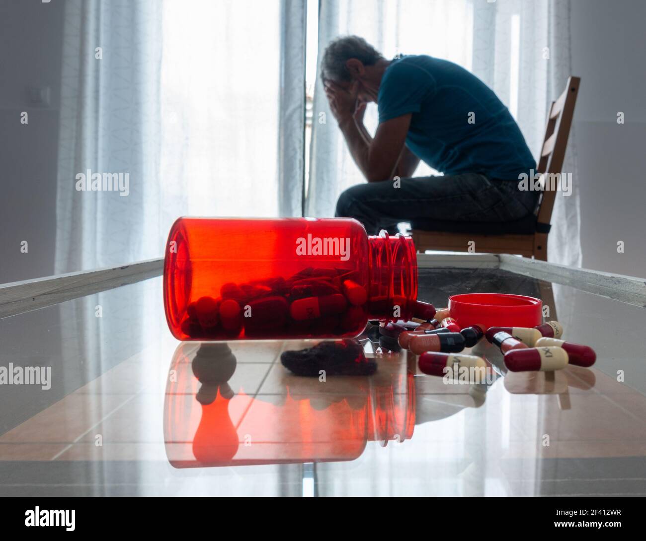 Mature man (63 years old) with head in hands near window with bottle of pills on table. Male depression, mental health, mental illness... concept Stock Photo