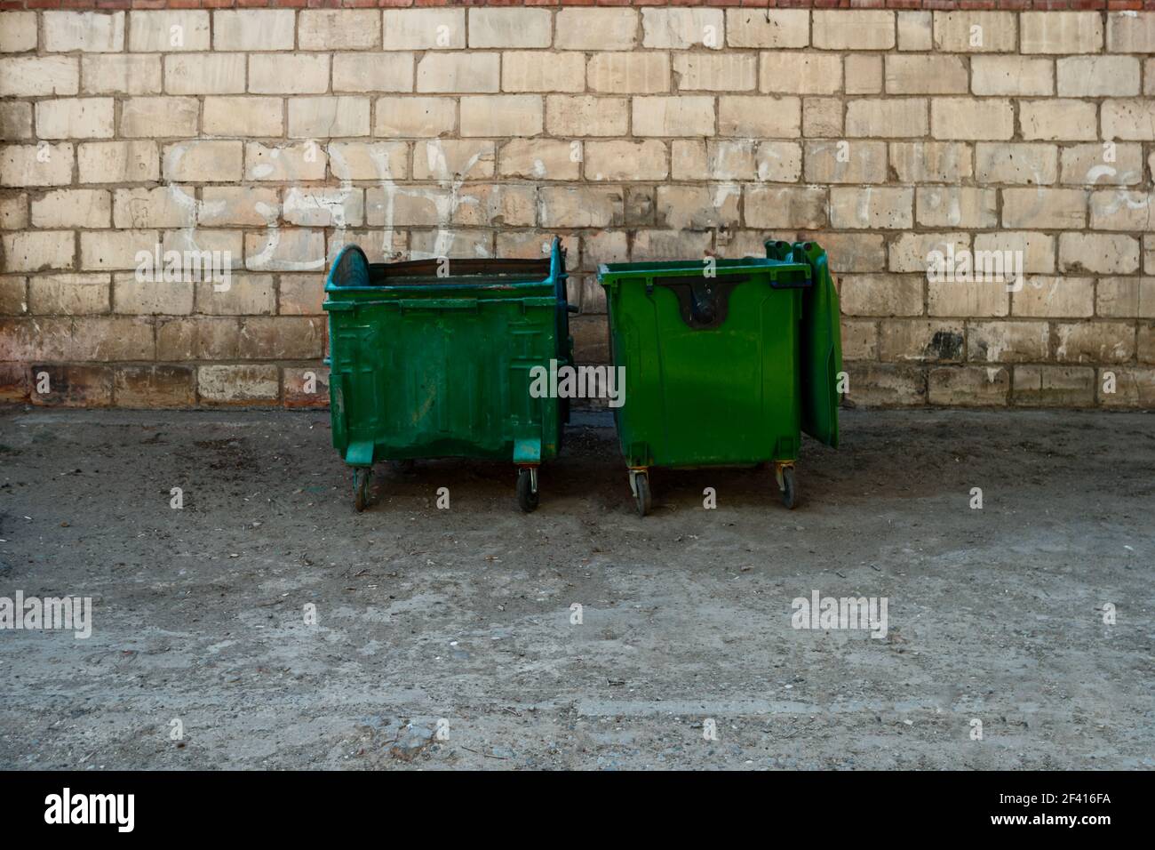 Plastic large trash cans with the lids up and garbage inside against a  brick orange wall. Big green and grey plastic dumpsters on a city street.  Waste Stock Photo - Alamy