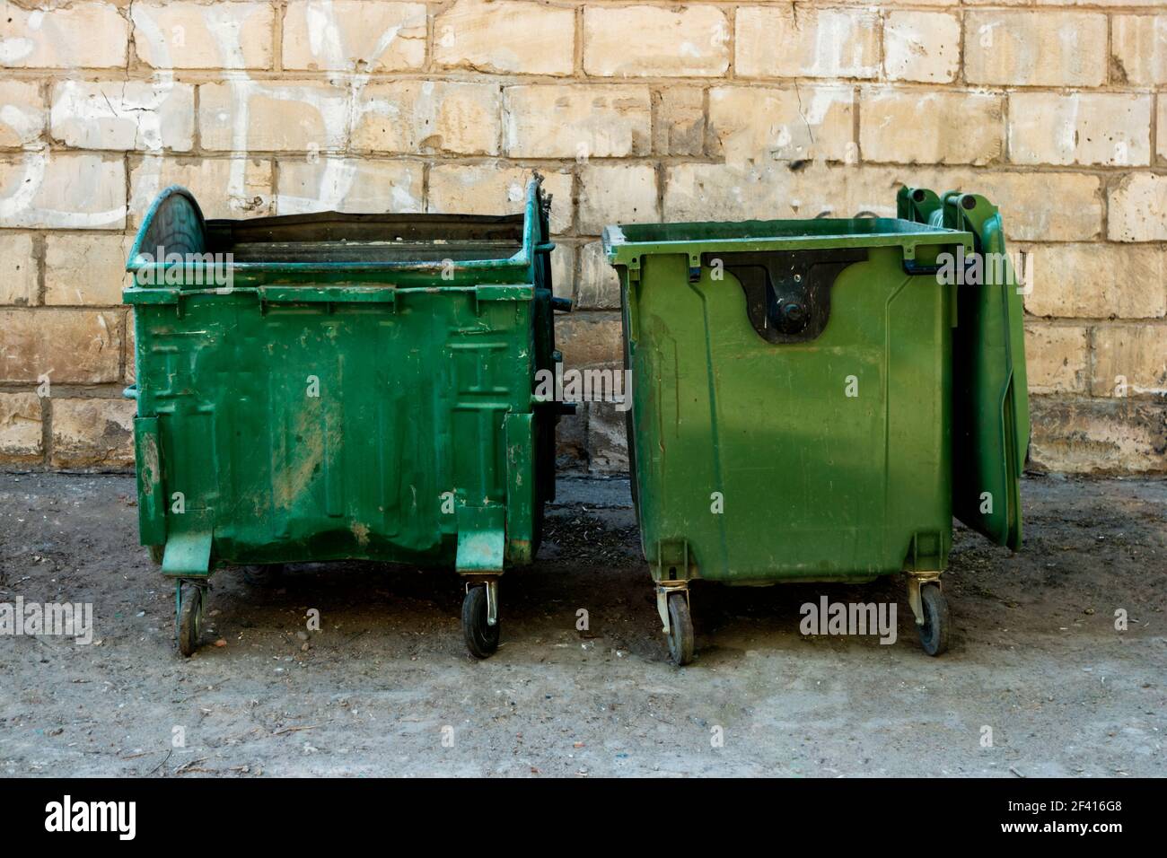 Plastic large trash cans with the lids up and garbage inside against a  brick orange wall. Big green and grey plastic dumpsters on a city street.  Waste Stock Photo - Alamy