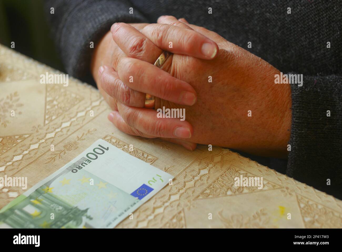 Hands of senior lady and 100 euro banknote on table in front her Stock Photo