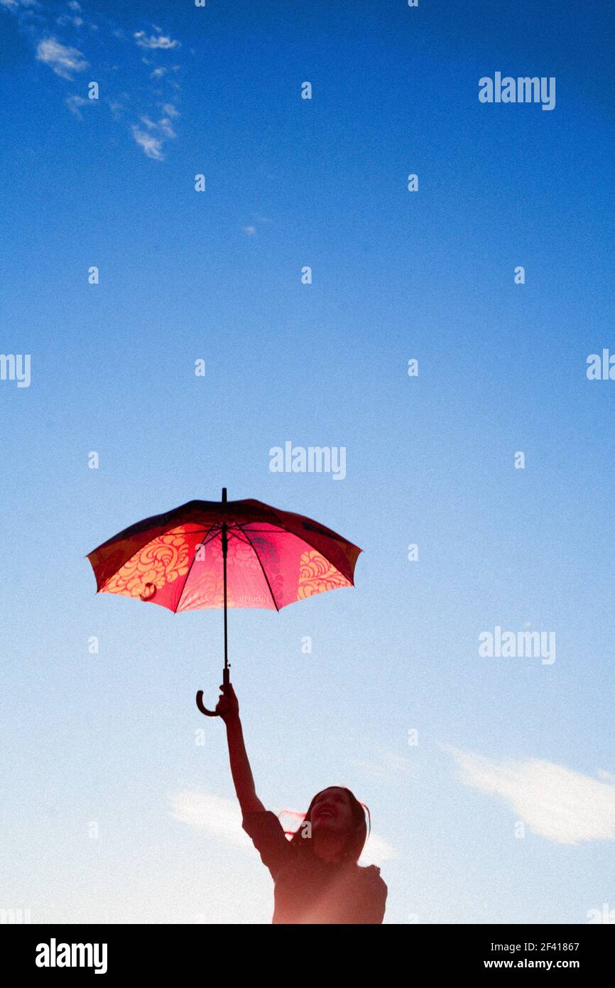 Beautiful young woman holding umbrella over clear sky. Freedom relax. Clear sky with gradient. Vintage looking image, backlit. Stock Photo