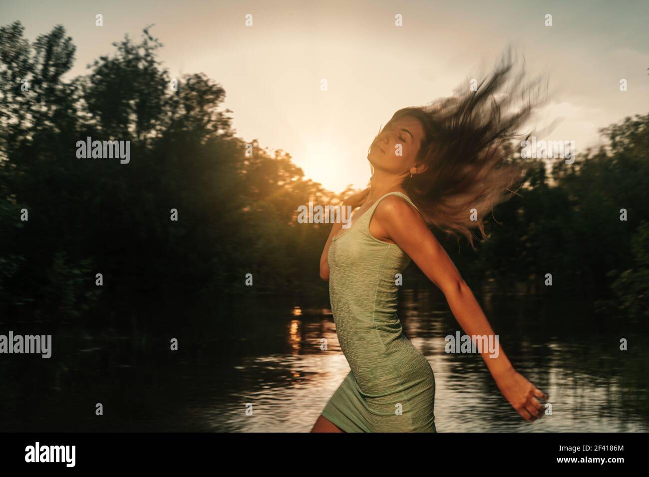 Beautiful blonde girl with long hair in short dress running at sunset on the river side with her hair flying in the air. Beautiful blonde girl with long hair in short dress running at sunset on the river side with her hair fly in an air Stock Photo