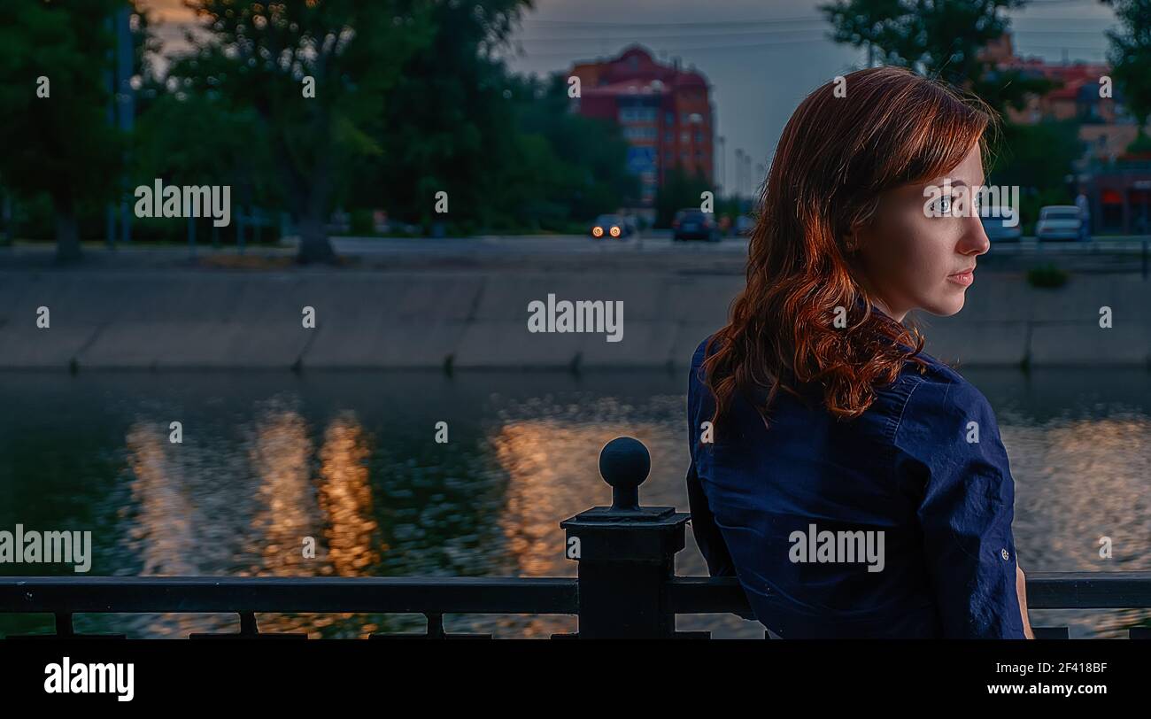 Young beautiful woman with red hair in profile shot against the night Moscow Skyline. Beautiful woman with red hair in profile shot against the night Moscow. Stock Photo