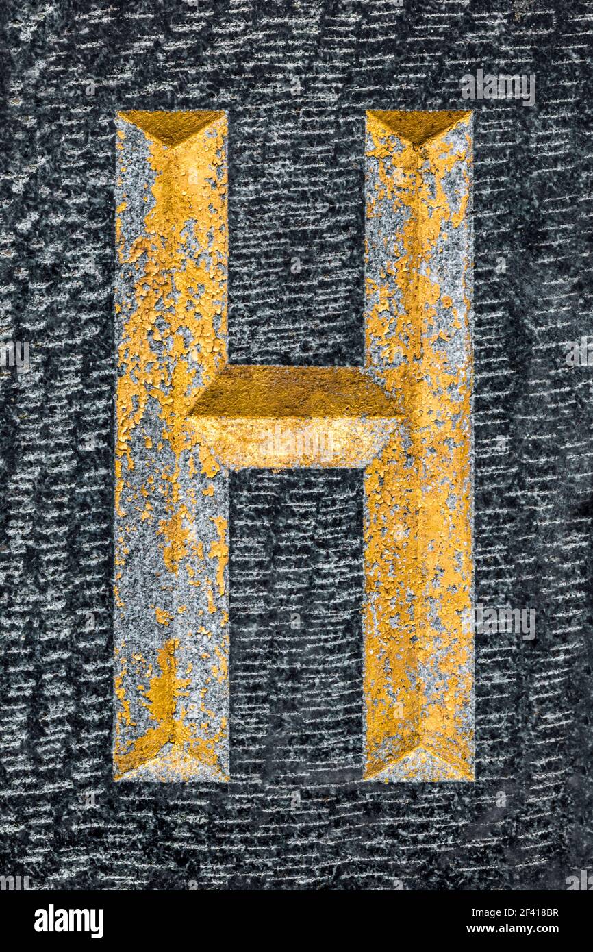 Golden weathered letter H on black granite Stock Photo