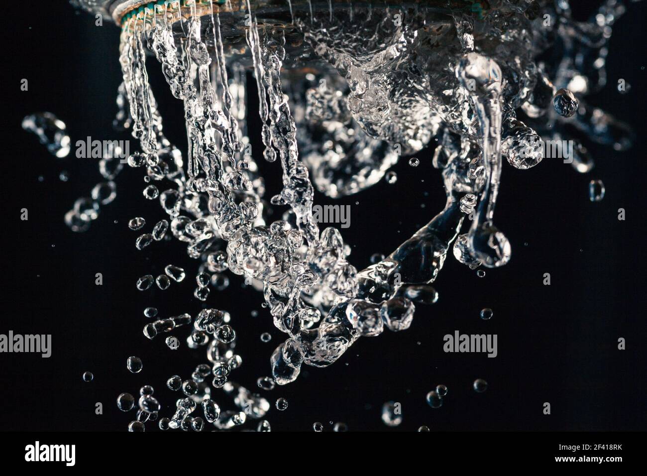 Water drops levitating about shower head on black background. Water
