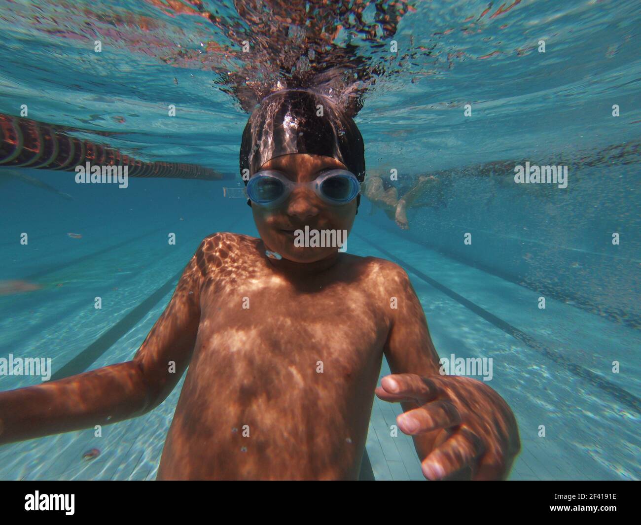 Boy underwater in goggles looking at camera, diving in swimming pool