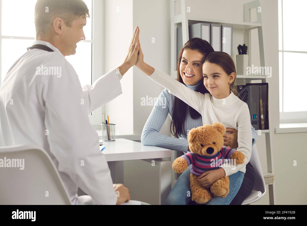 Happy little girl patient gives five smiling male pediatrician after medical examination. Stock Photo