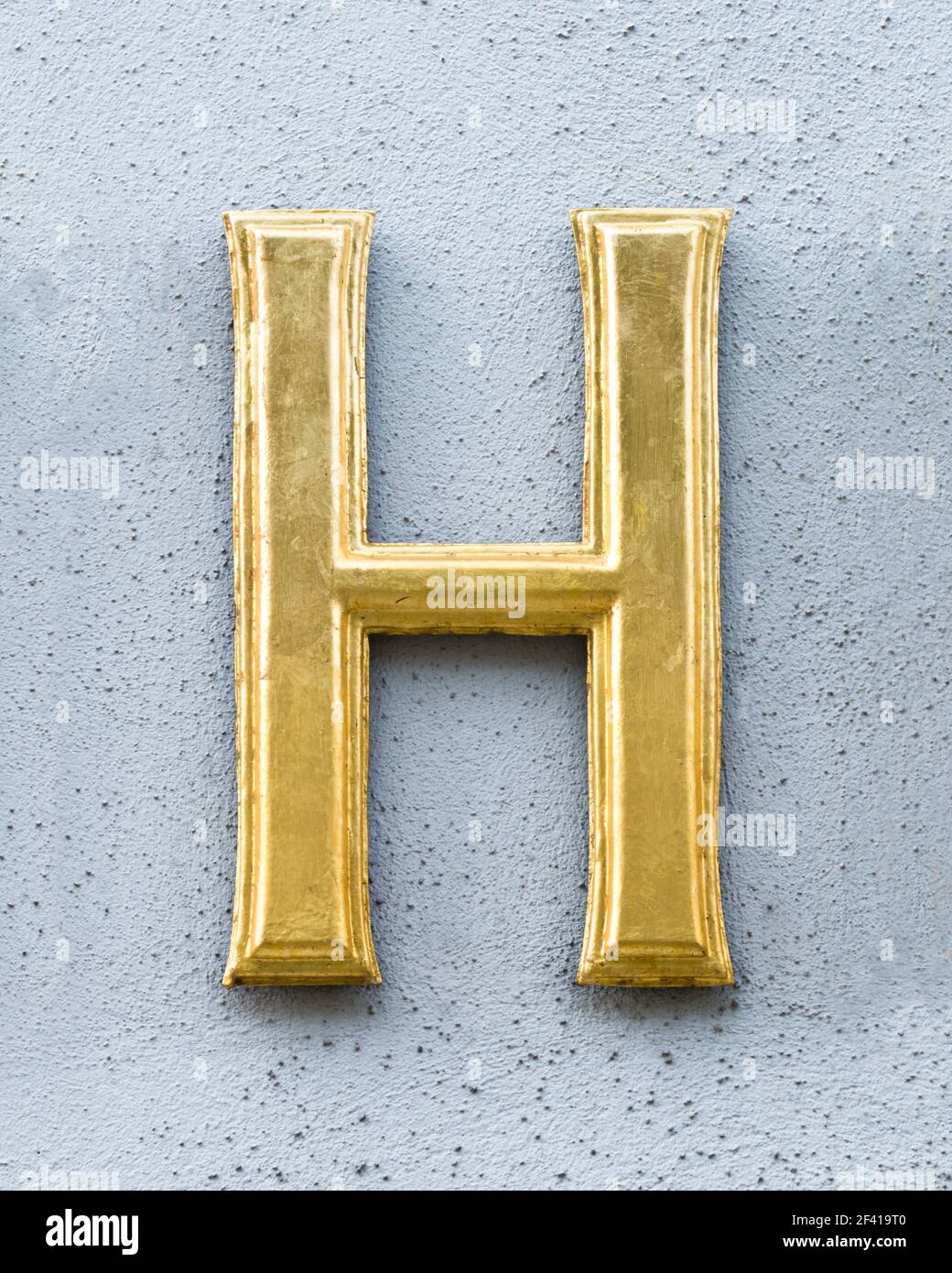 Golden letter H on a light grey wall Stock Photo