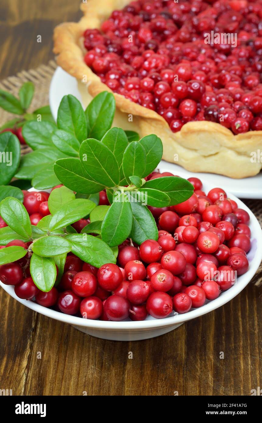 Ripe lingonberry in bowl and cowberry pie on wooden table Stock Photo