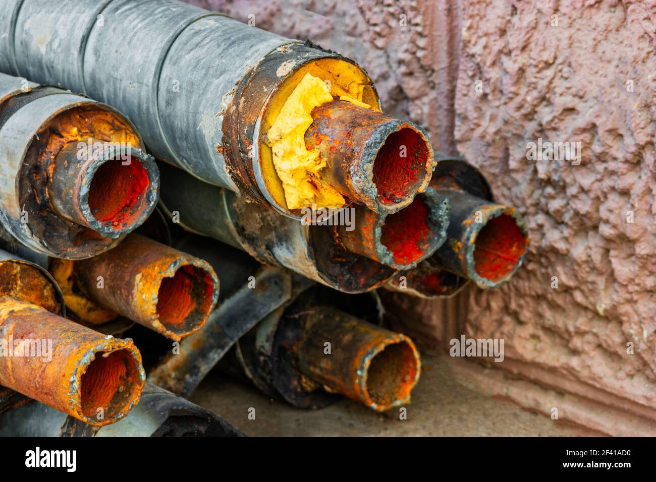 Water Pipeline repair. Rusty steel pipe with insulation on the construction site in a plastic foam tube wrapper lying on the yard in a bunch horizontally. Rusty old pipeline stacked up near the wall. Water Pipeline repair. Rusty steel pipe with insulation on the construction site in a plastic tube wrapper lying on the yard in a bunch horizontally. Rusty old pipeline stacked up Stock Photo