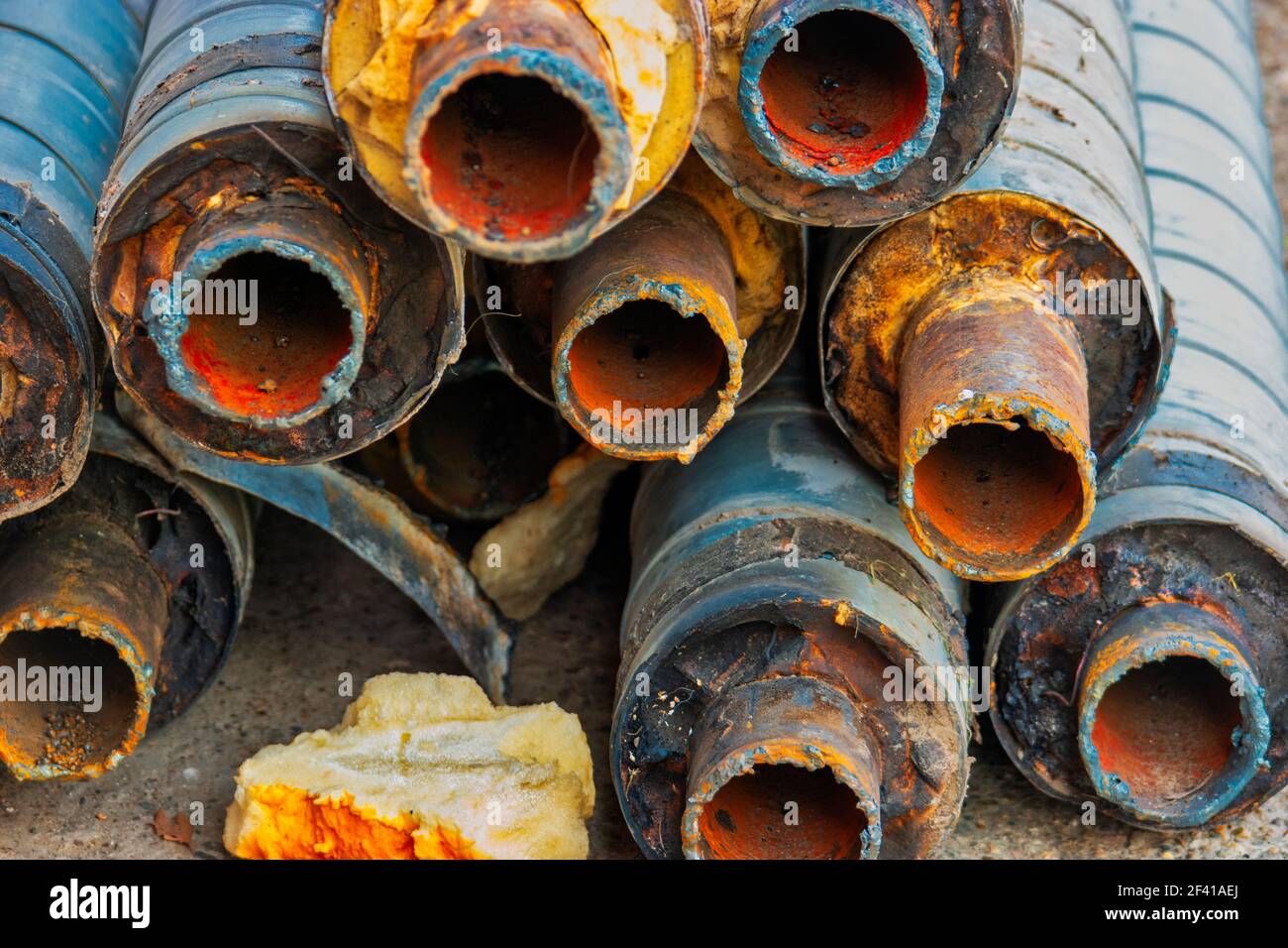 Water Pipeline repair. Large rusty steel pipe with insulation on the construction site in a plastic tube wrapper lying on the yard in a bunch horizontally. Rusty old pipeline stacked up. Water Pipeline repair. Large rusty steel pipe with insulation on the construction site in a plastic tube wrapper lying on the yard a bunch horizontally. Rusty old pipeline stacked up Stock Photo