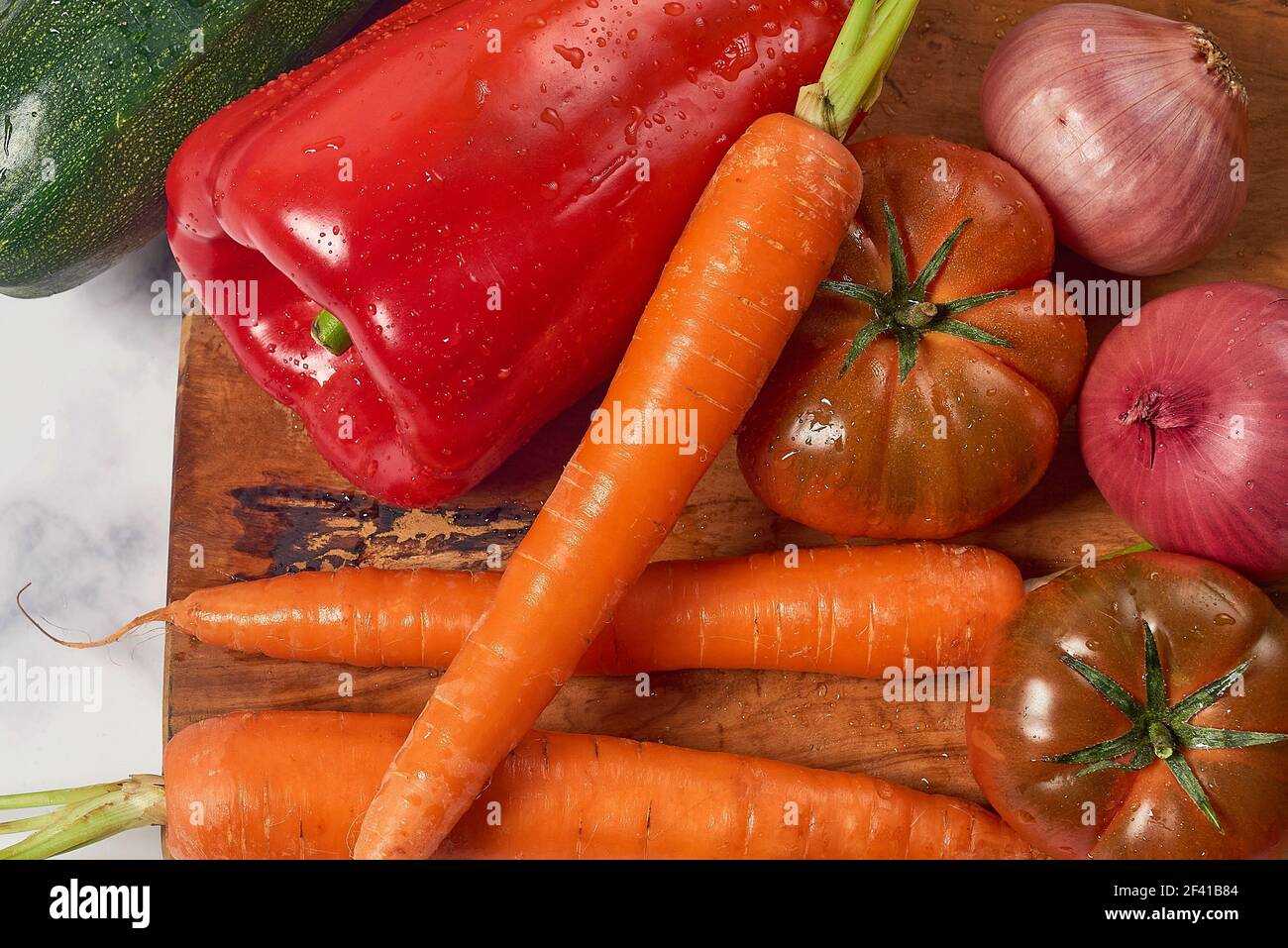 Various greens and vegetables on wooden kitchen table a white marble
