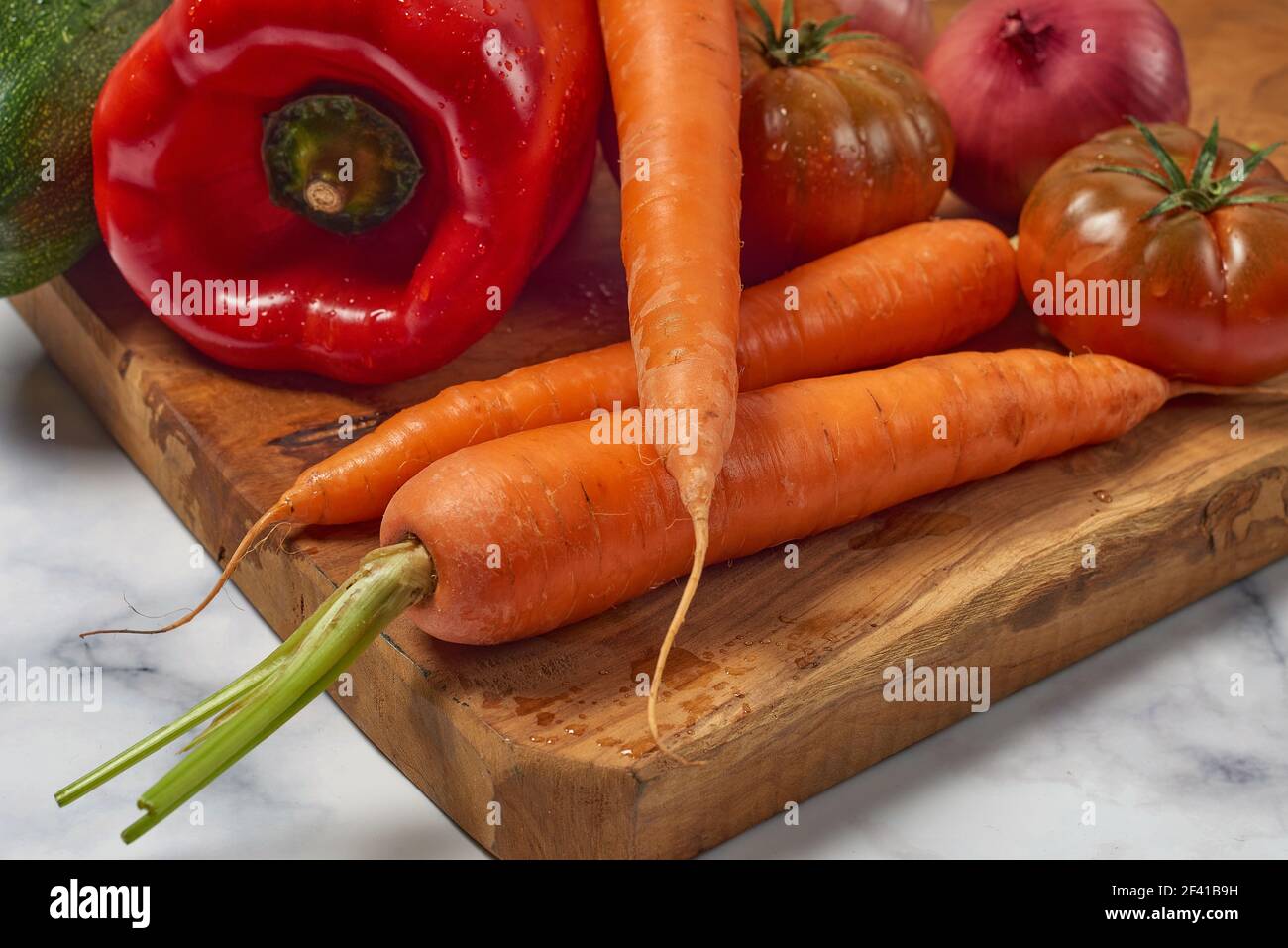 Various greens and vegetables on wooden kitchen table a white marble
