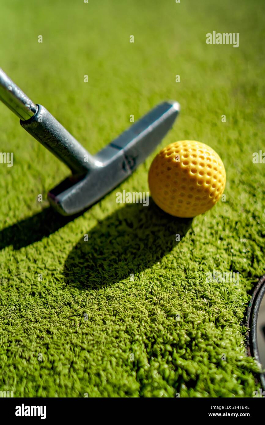 Mini Golf yellow ball with a bat near the hole at sunset Stock Photo