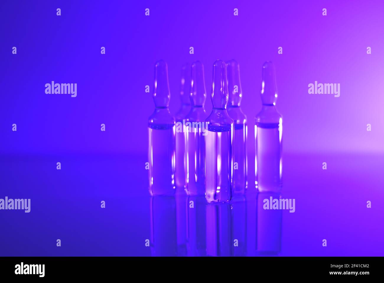 Medicine and Pharmacology concept. Vaccine ampoules. Glass transparent ampoules set in purple light.Biotechnology and Science.Ampoules with solution Stock Photo