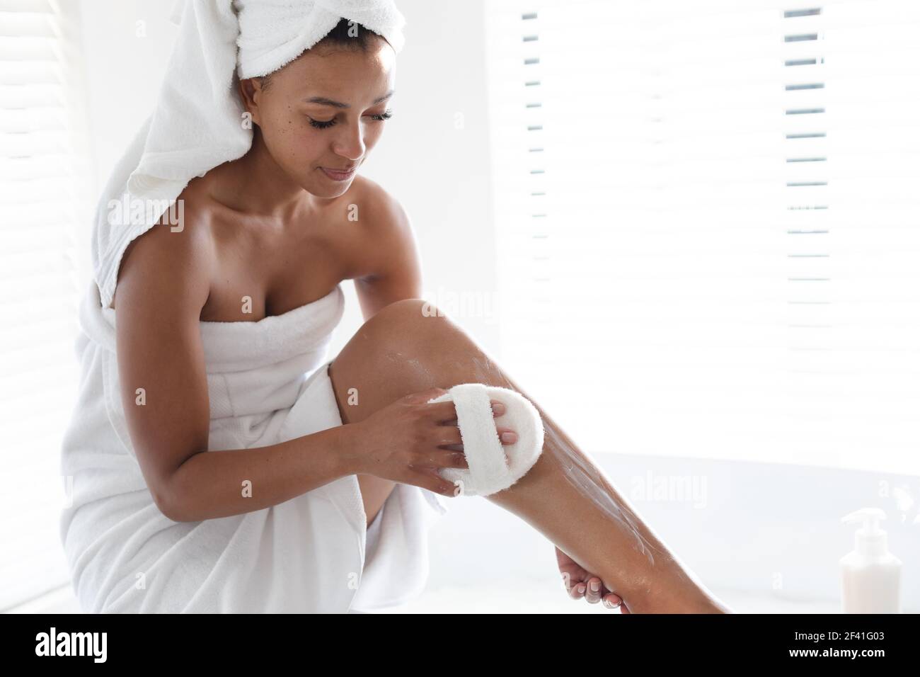 African american woman massaging her legs with loofah pad in bathroom Stock Photo