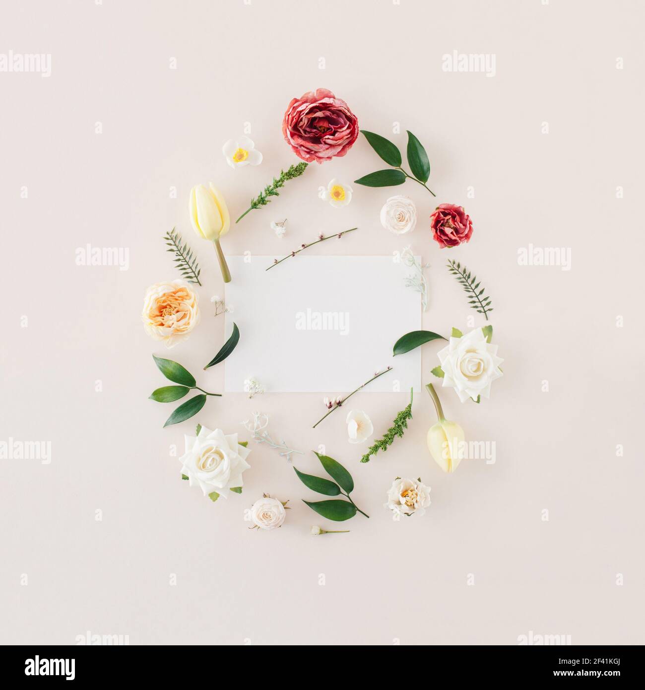 Creative spring Easter  frame made with  colorful  spring flowers and green leafs with  paper card note over pastel beige  background.  Minimal flat l Stock Photo