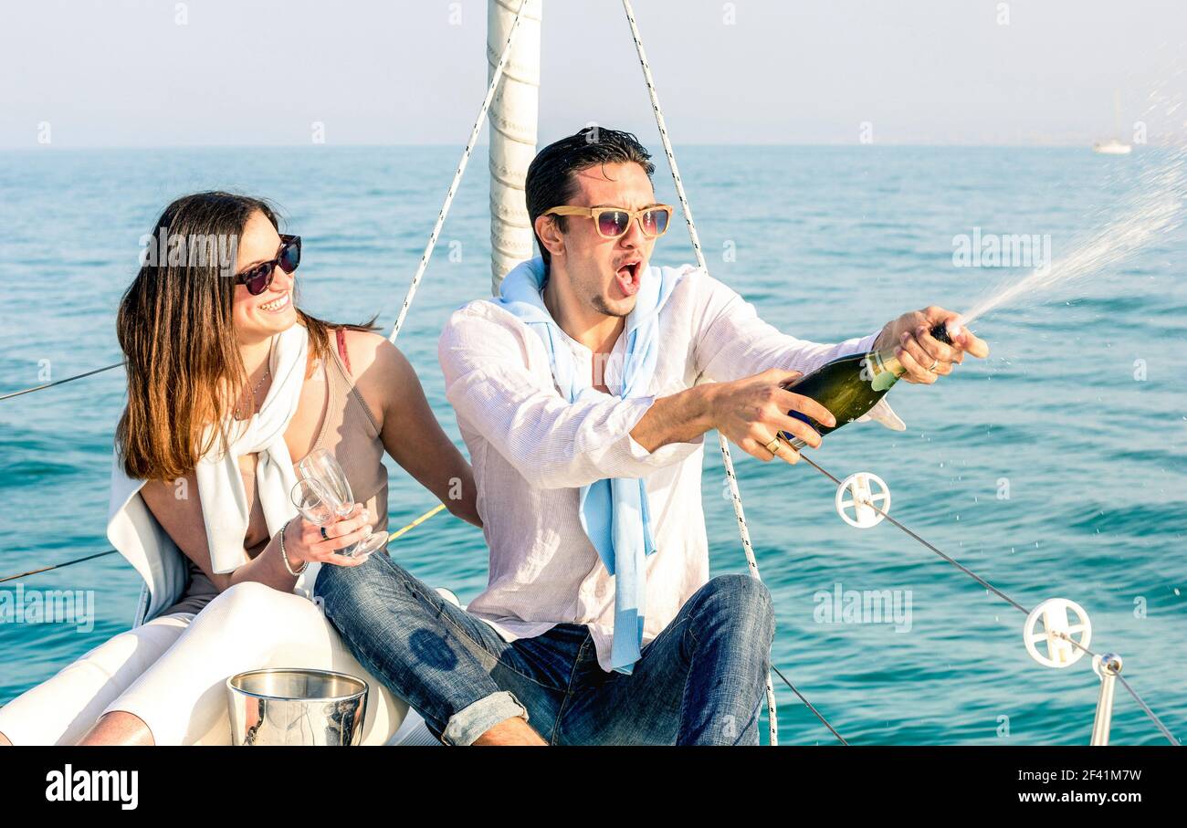 Young couple in love on sailing boat cheering with champagne wine bottle - Happy girlfriend birthday party cruise travel on luxury sailboat Stock Photo