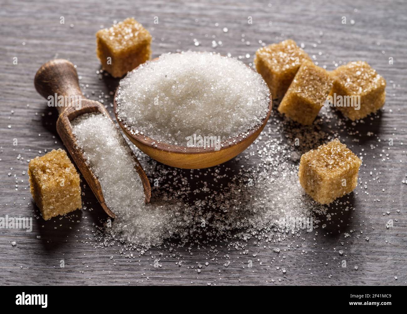 Granulated table sugar in wooden bowl and in the spoon and sugar cubes