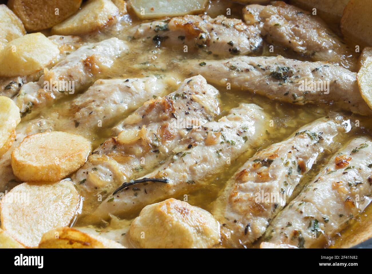Close-up of chicken fillets with garlic and spices in a green sauce accompanied by baked potatoes. Healthy food. Stock Photo