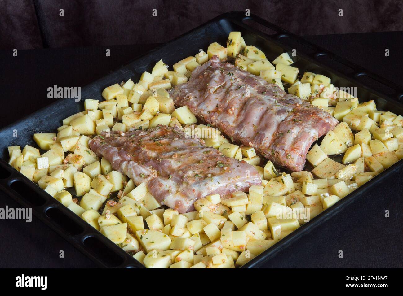 Strips of fresh pork rib bathed in a sauce of garlic, oil, vinegar, and oregano surrounded by potatoes on a baking sheet. Fresh food and raw meats. Stock Photo