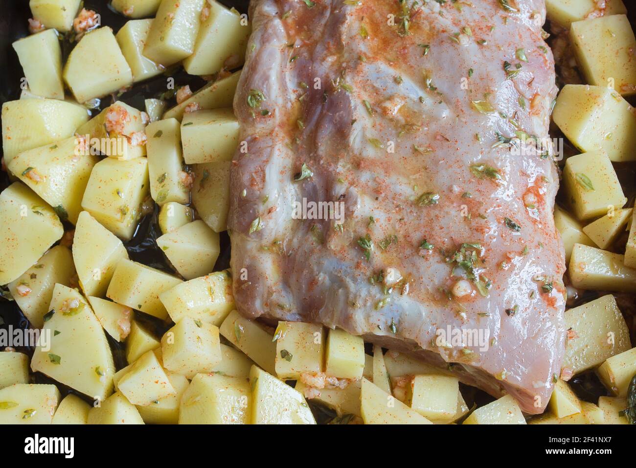 Overhead view of fresh pork ribs and potatoes cut into squares bathed in a sauce of garlic, oil, vinegar, and oregano. Fresh food and raw meats. Stock Photo
