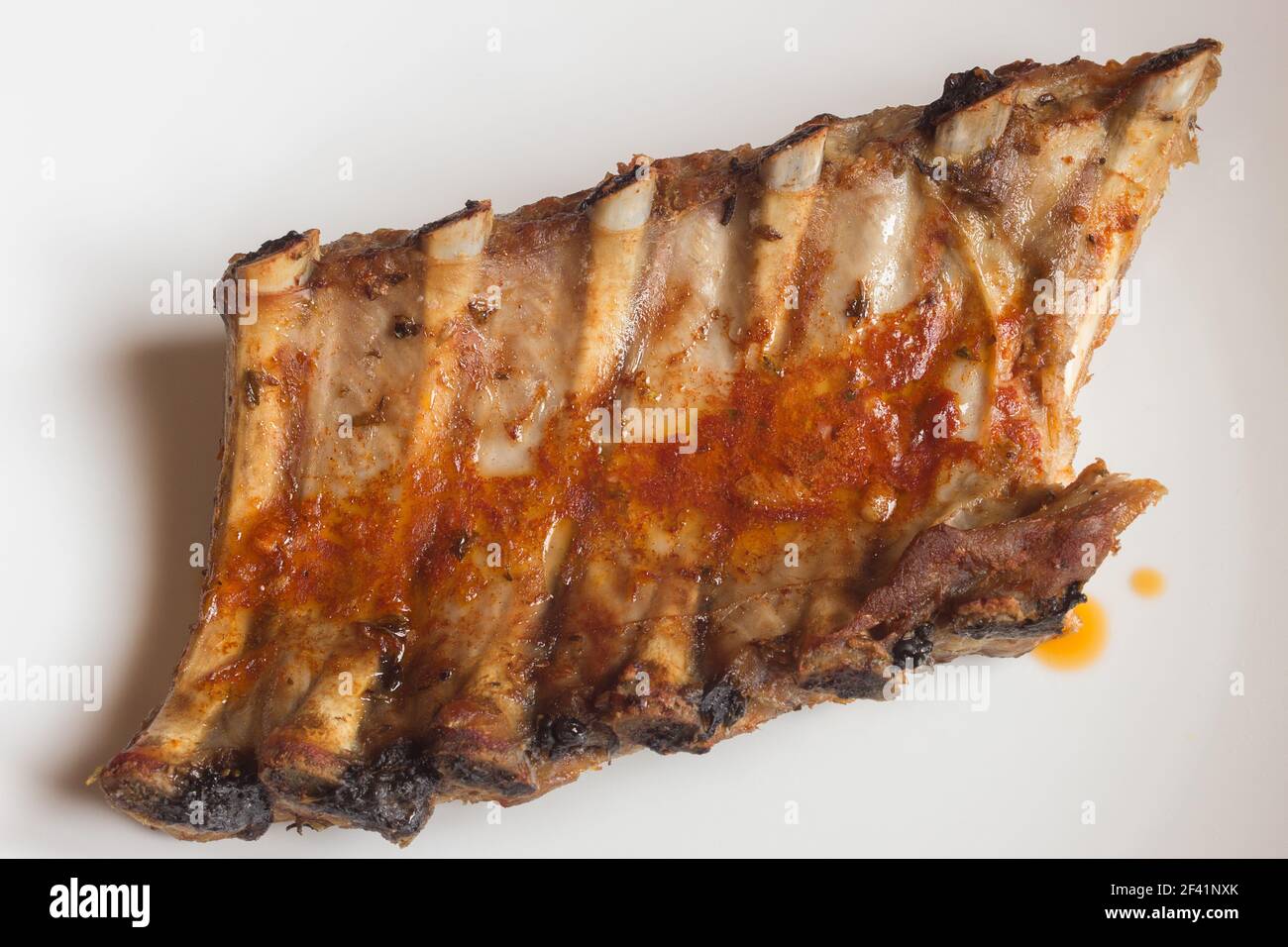 Overhead view of baked pork ribs dipped in a spicy sauce on white background. Tasty homemade meat recipes. Stock Photo