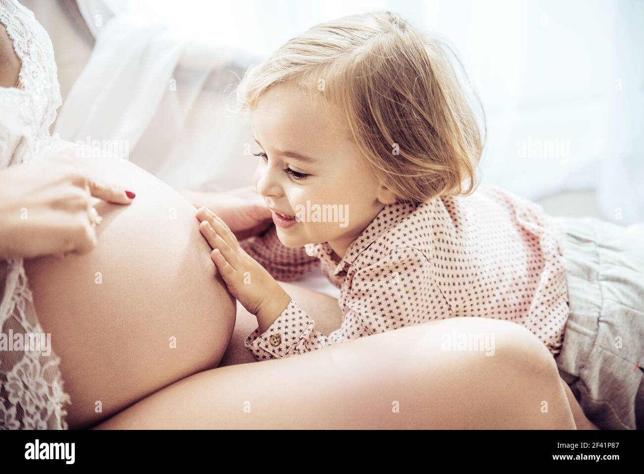 Charming, little daughter touching a pregnant mother&rsquo;s belly Stock Photo