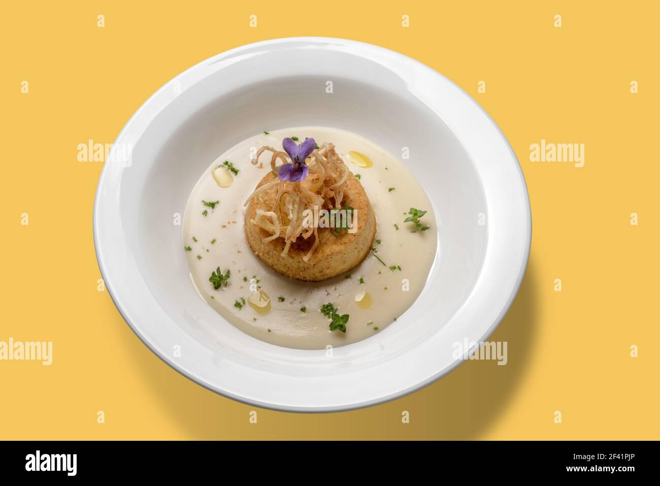 savory flan of leeks in cream cheese and olive oil, in white plate isolated on yellow background, top view Stock Photo