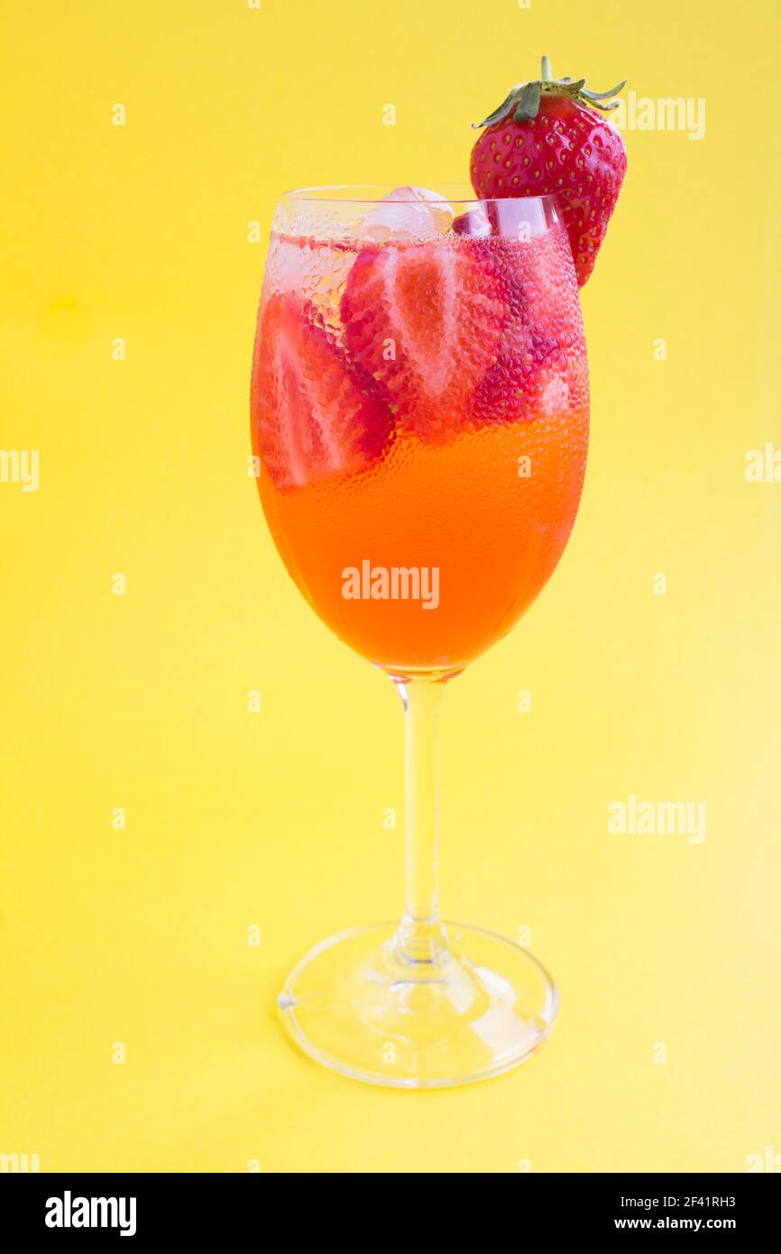 Cocktail drink with strawberry and ice in a wineglass  on the yellow  background. Location vertical. Closeup. Stock Photo