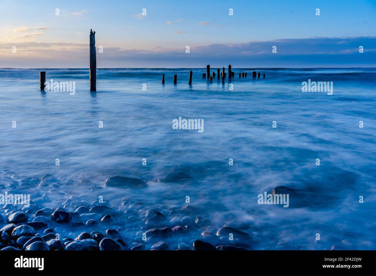 at sunset old wooden poles in the sea that are remnants of ancient times when fishermen fished from the shore with their small wooden fishing boats Stock Photo