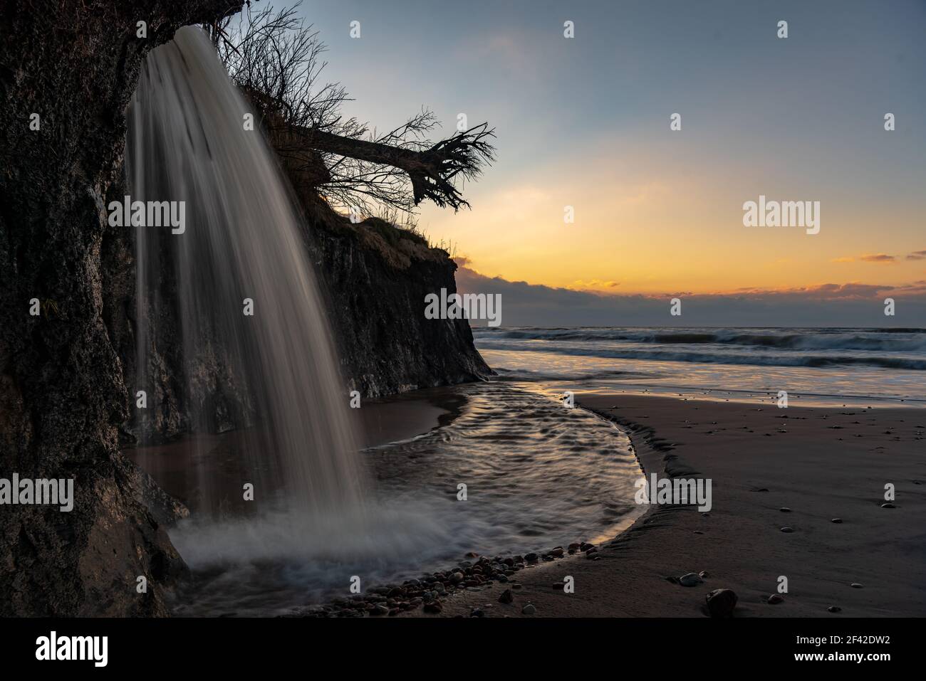 sunset waterfall on the floor by the sea with a beautiful small river estuary in the wide sea waters and clouds on the horizon Stock Photo