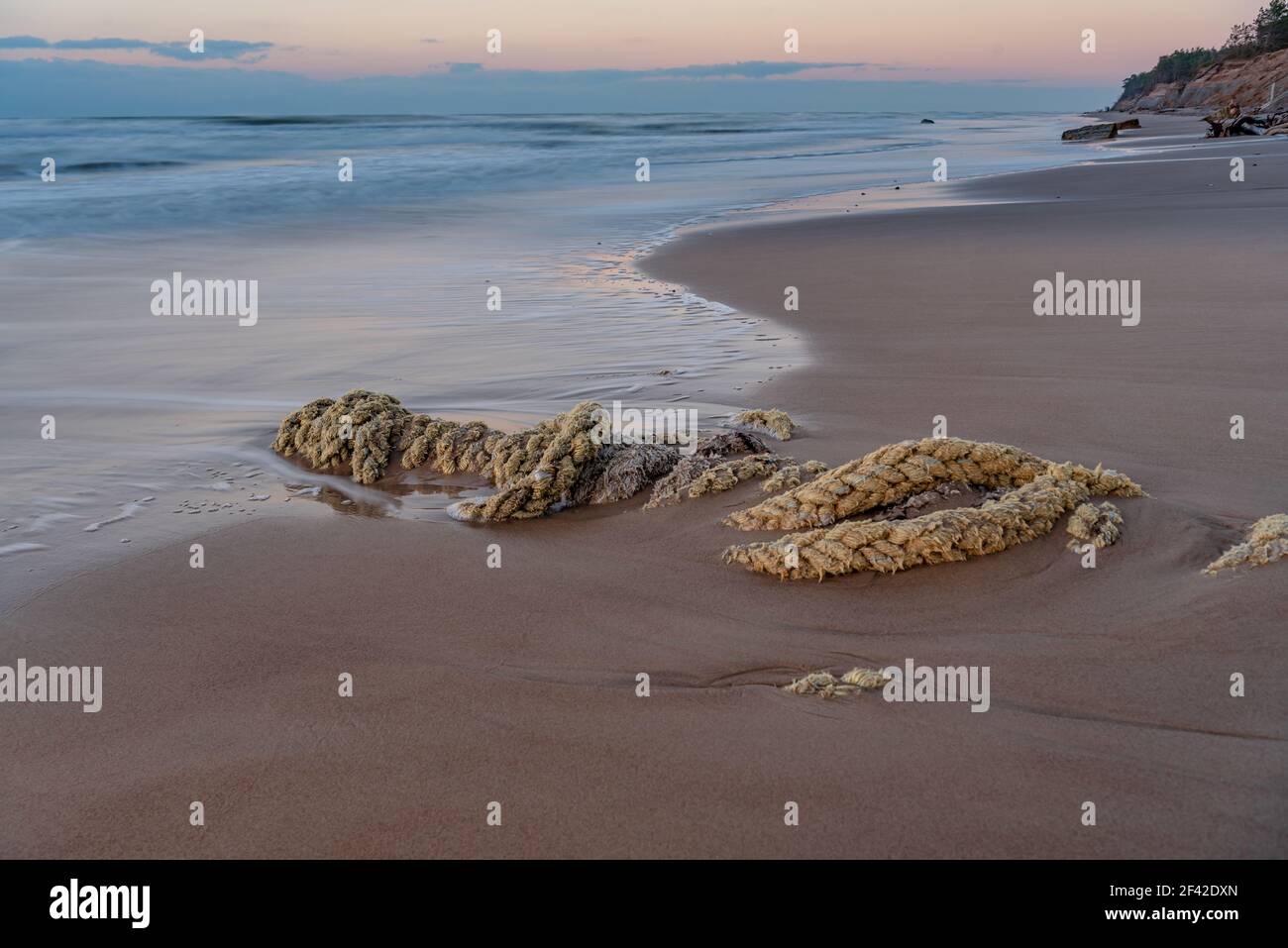 rope washed up in the sand by the sea shore is partially covered with light sand in the sunny Stock Photo