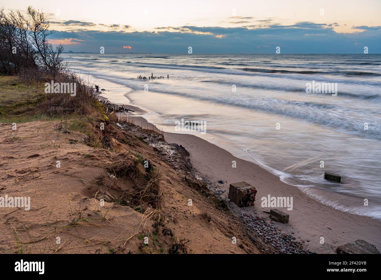 cliff at sunset by the sea and the remains of the building wall left on the beach after the cliff collapsed and the house collapsed Stock Photo