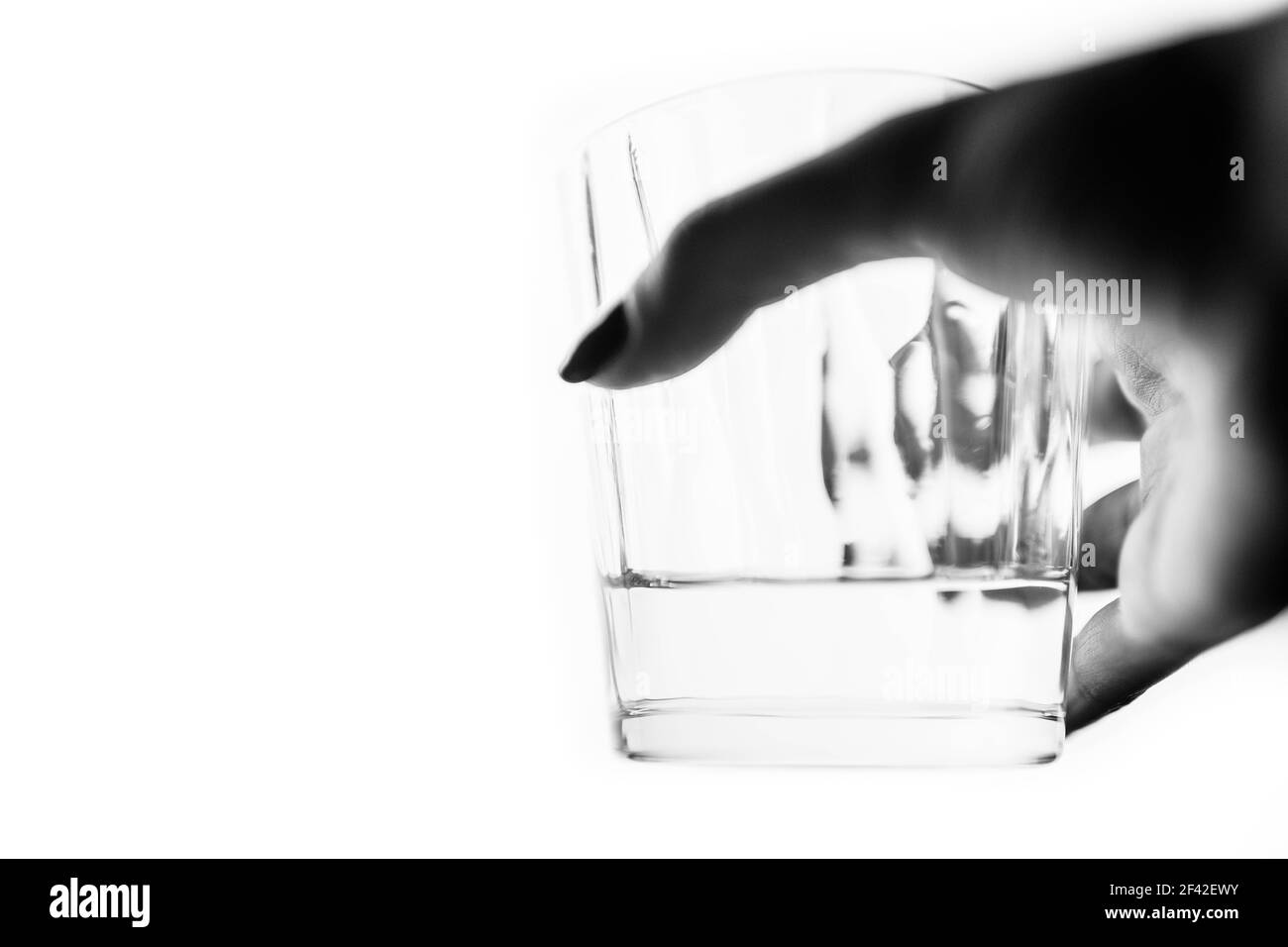 A glass of water in a female hand on a white isolated background. Side view, selective focus, bw photo Stock Photo
