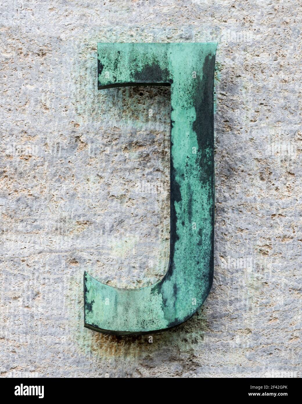 Metal letter J covered with verdigris on a natural stone wall Stock Photo