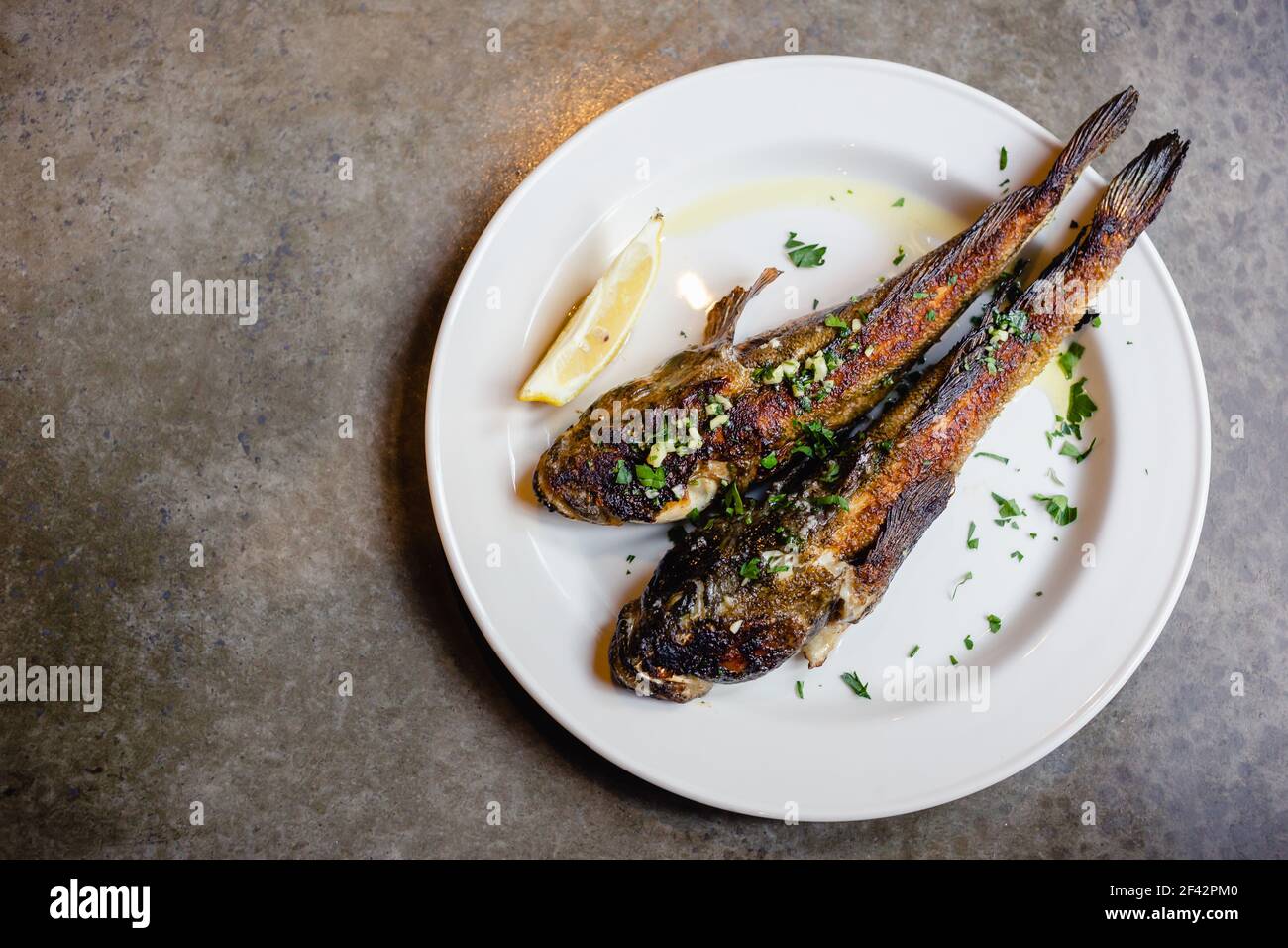 Two fried sea goby fish on white plate with lemon close-up. Mediterranean cuisine, junk food, tasty snacks for beer concept Stock Photo