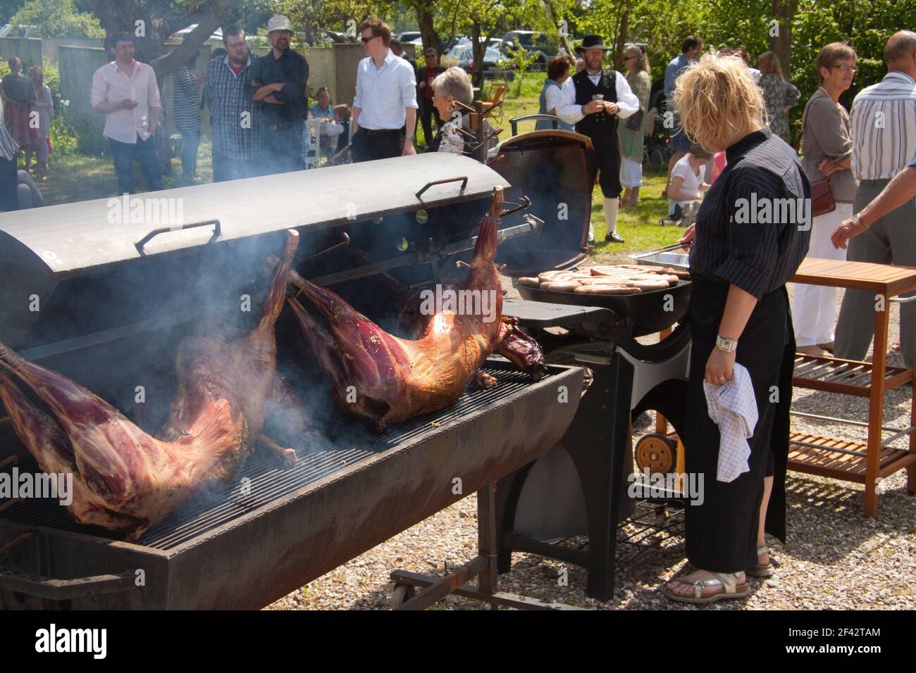 Female chef roasting whole pigs on a large grill at outdoor social  arrangement with crowd of people standig in the background. Smoke coming up  from bb Stock Photo - Alamy