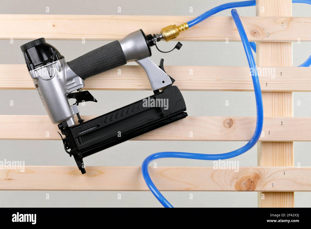 A compressed air nailer with pressure hose on a wooden fence Stock Photo