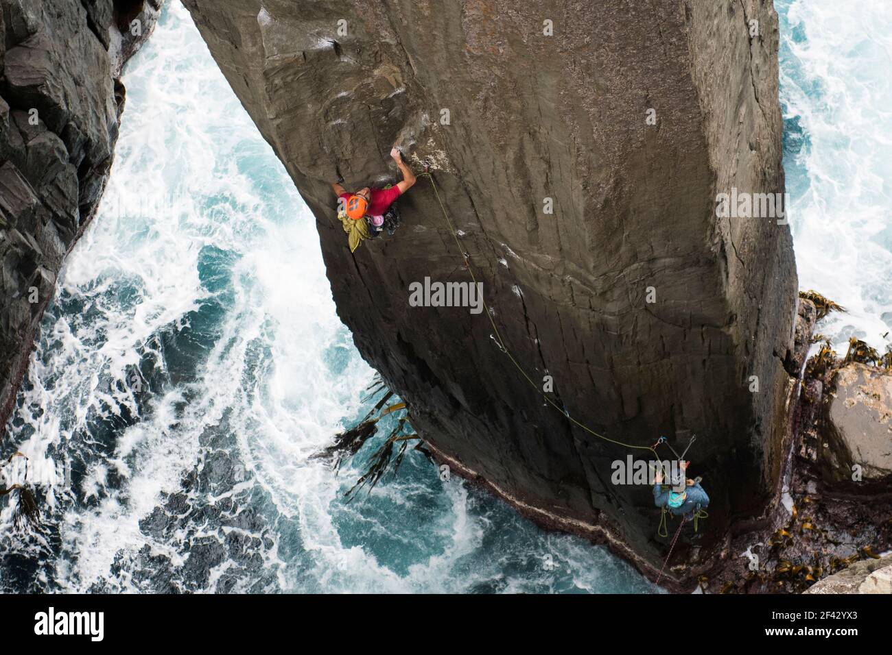 Rock climber grabs a crimp as he climbs a rock pilar out of the ocean
