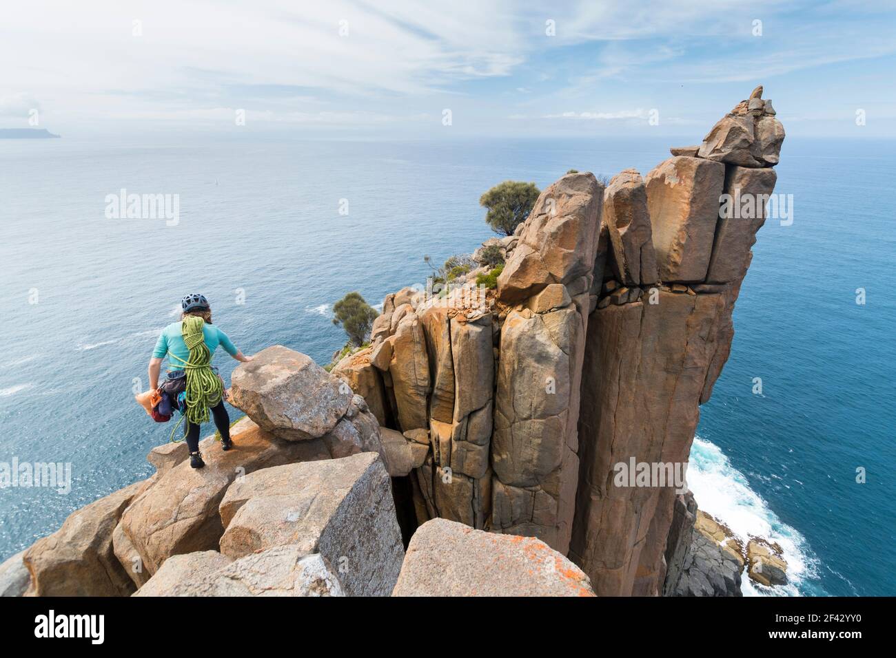 Female adventurer heads off into the unkown, armed with ropes and climbing gear, as she explores dolerite rock columns in the  sea cliffs of Cape Raoul, in Tasmania, Australia. Stock Photo