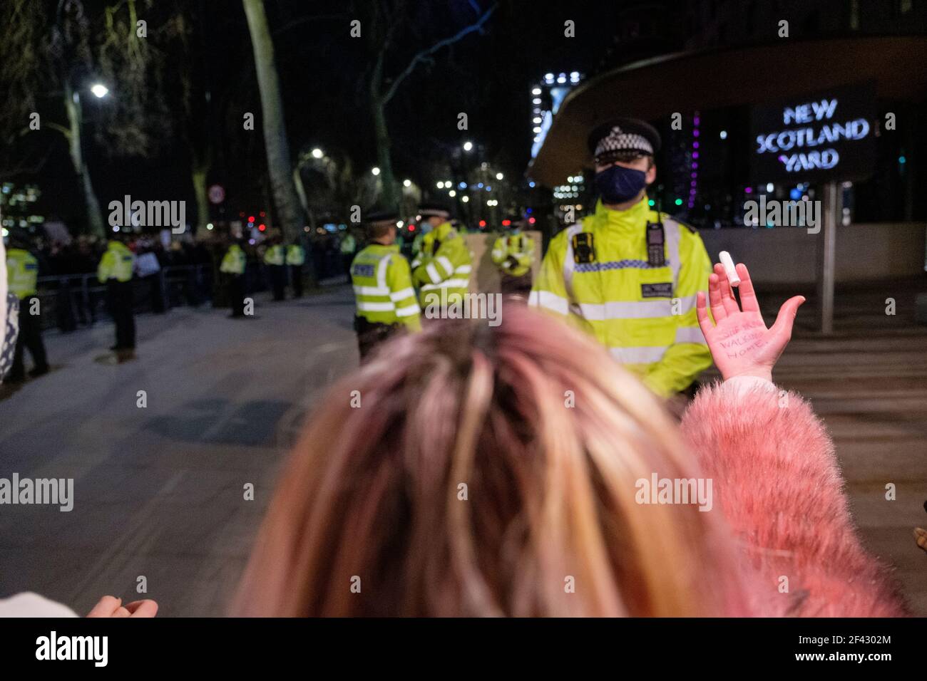 London, UK. 16th March, 2021. Woman holds a tampon to a police officer in  front of New Scotland Yard. "She was just walking home" written in her  hand. Thousands gathered in Parliament