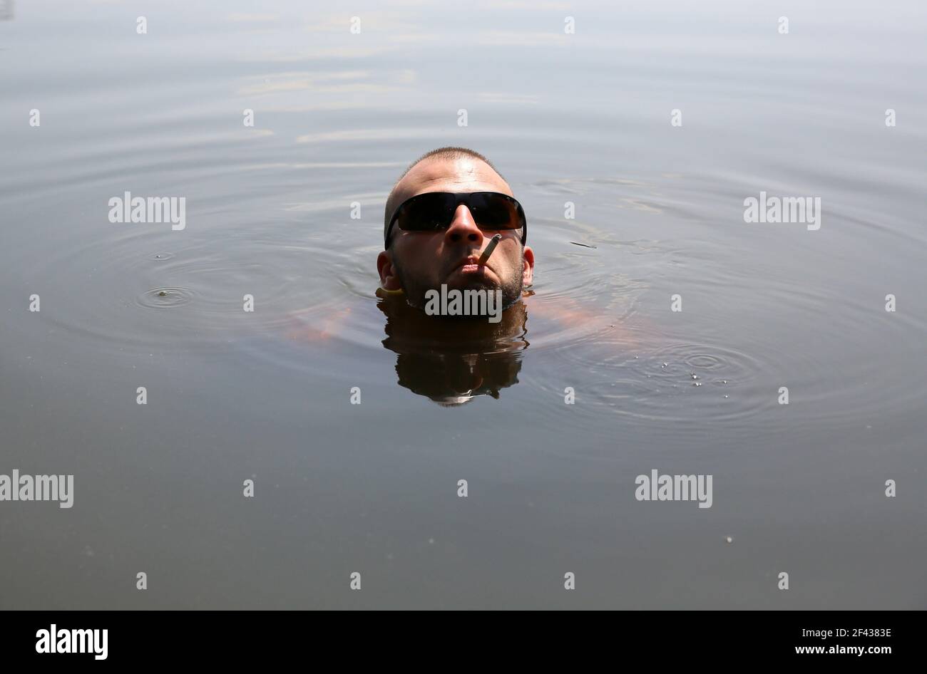 A man swims in a pond and relaxing smoking a cigarette Stock Photo