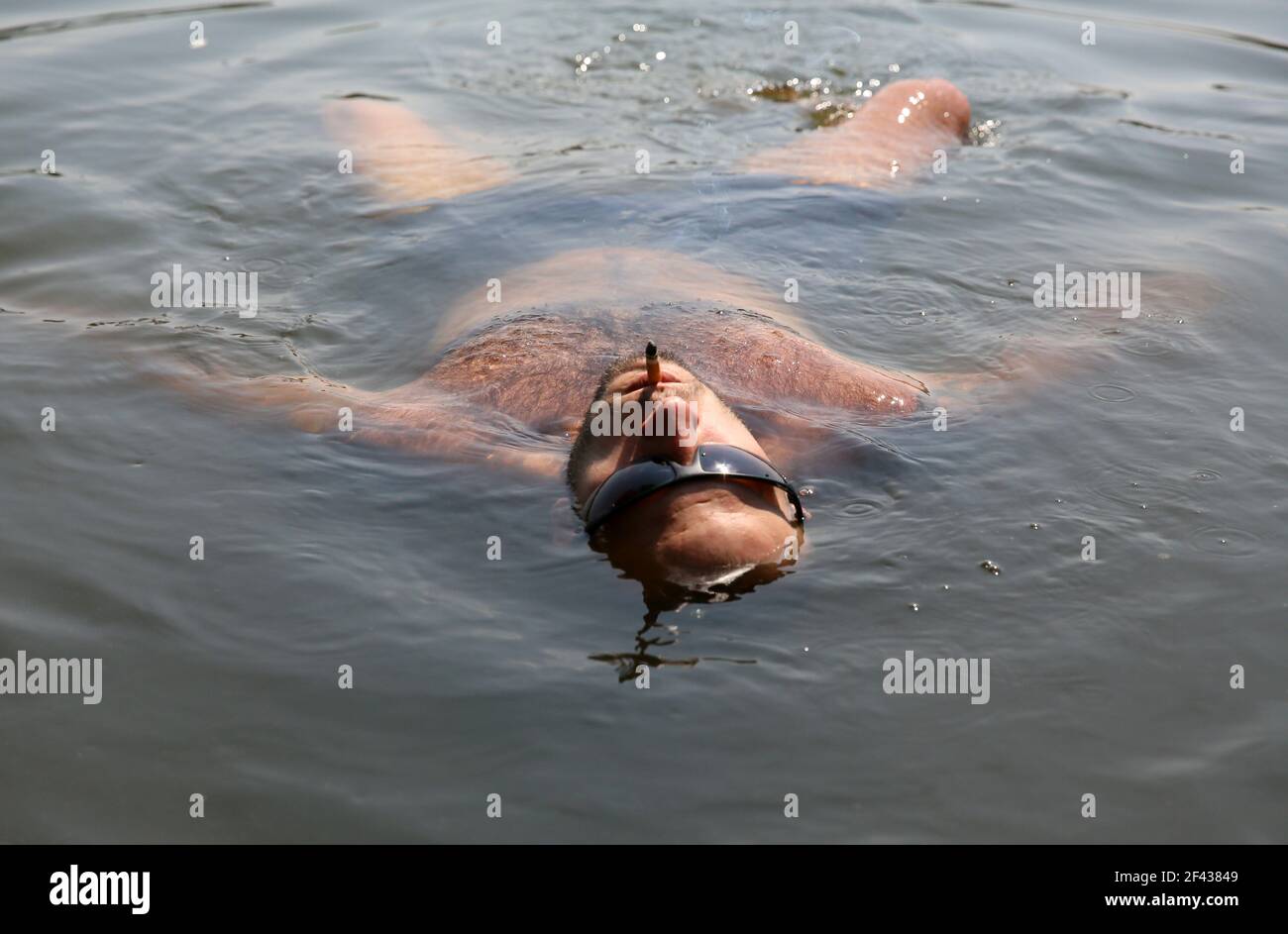 A man swims in a pond and relaxing smoking a cigarette Stock Photo