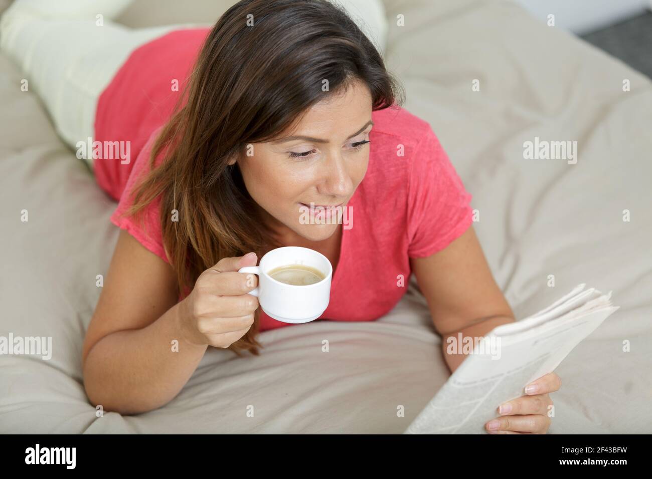woman layed on bed with a coffee reading a newspaper Stock Photo - Alamy